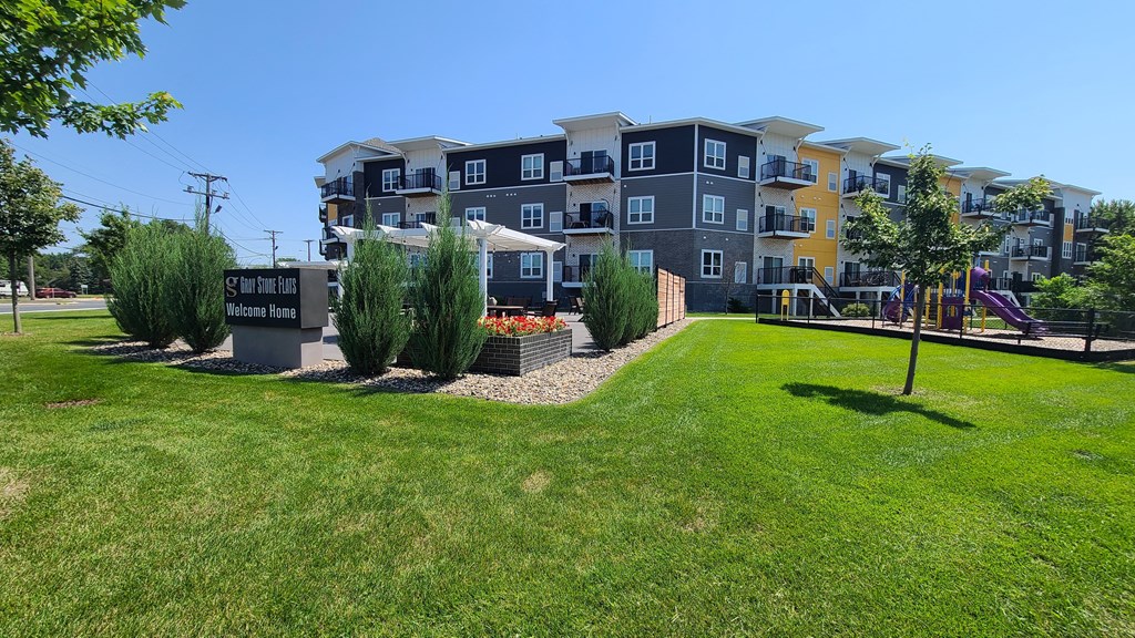 an apartment building with a green lawn and trees in front of it