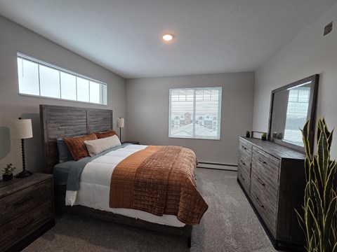 A bedroom with a large bed, a nightstand with a lamp, and a dresser with a mirror.