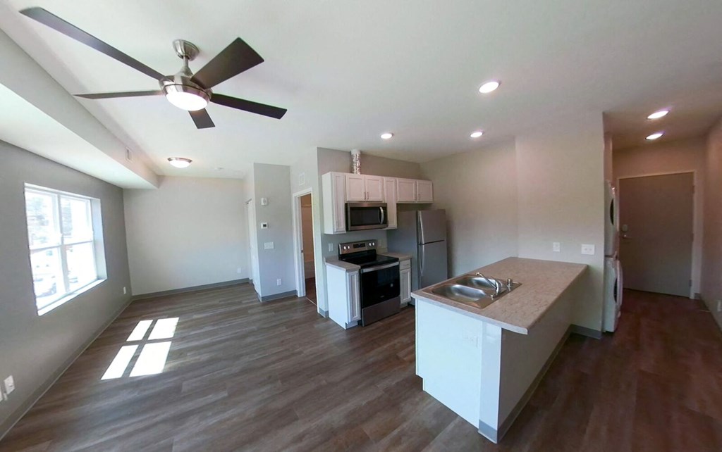 a living room with a kitchen and a ceiling fan