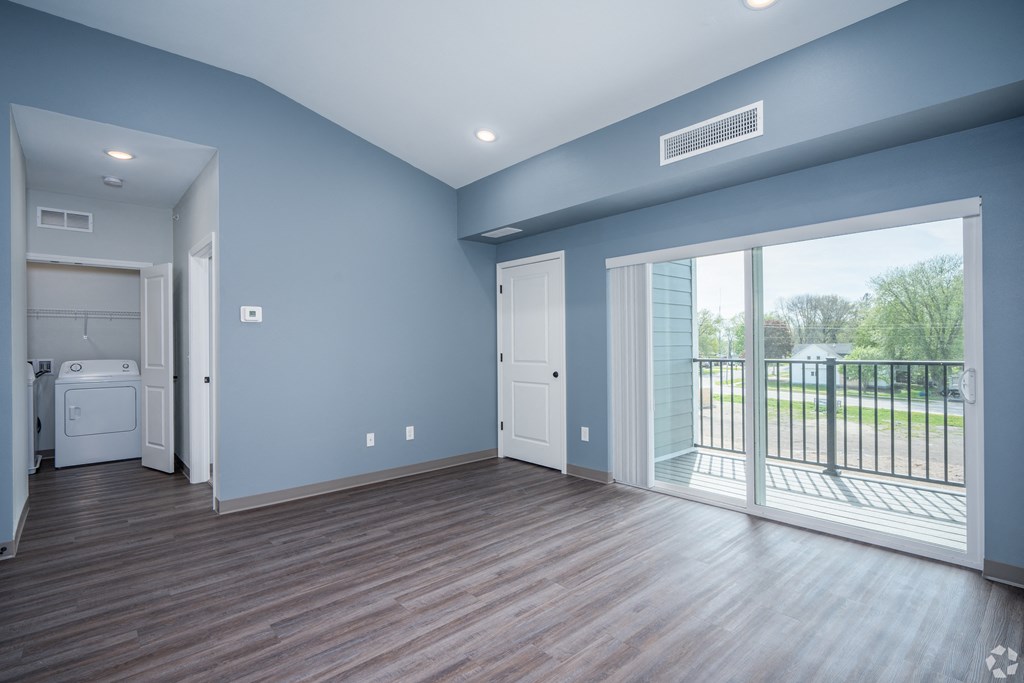 an empty living room with a large window and a door to a balcony