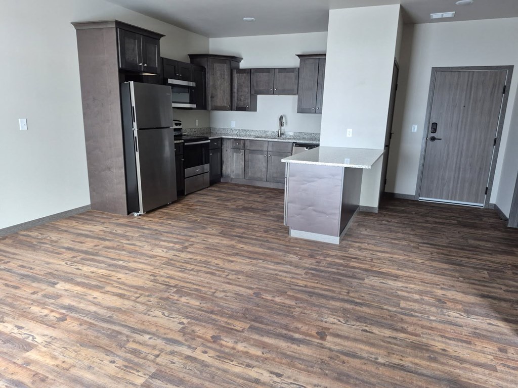 A kitchen with a black refrigerator and wooden floors.