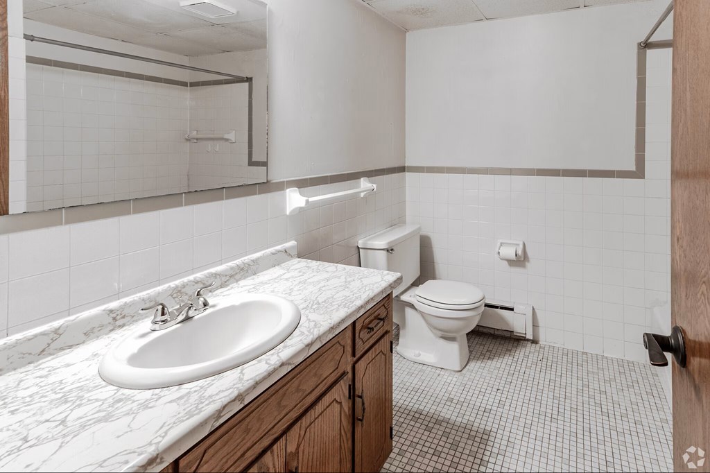 A white bathroom with a marble counter top and a toilet.