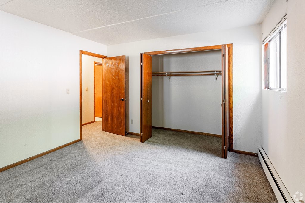 A room with a carpeted floor, a white wall, a window, and a wooden door.