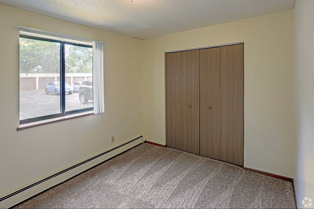 A room with a carpeted floor, a sliding glass door, and a wooden wardrobe.