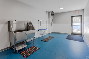 A room with blue flooring and white walls has a couple of sinks and a door with an exit sign above it.