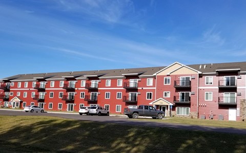 A row of red apartment buildings with cars parked in front.