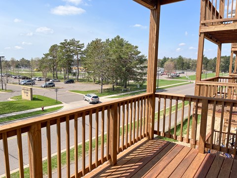A wooden balcony overlooks a parking lot and trees.