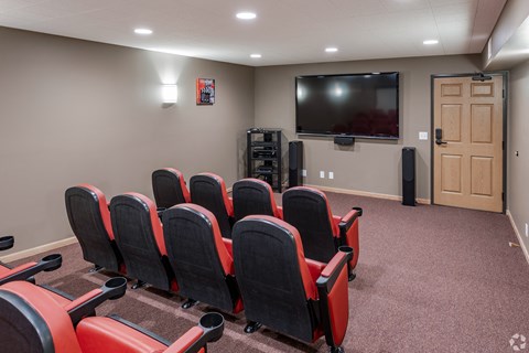 a small theater room with red chairs and a television