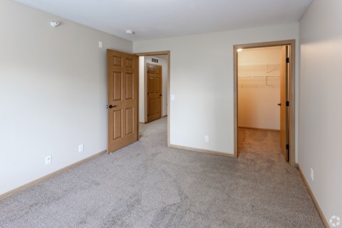 an empty living room with two doors and a hallway to a bedroom