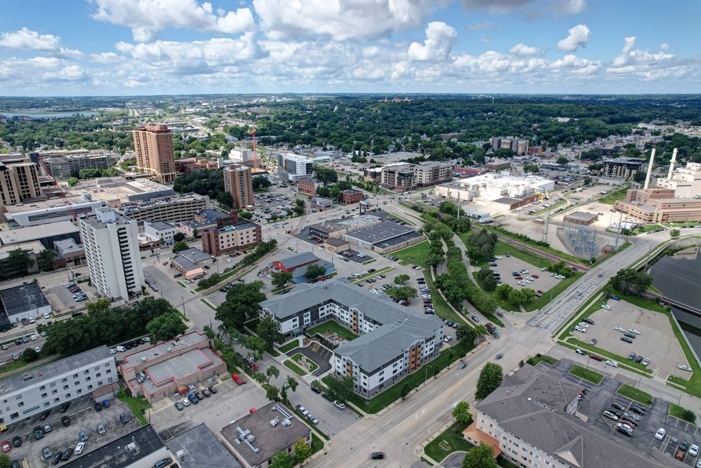 A cityscape with buildings, roads, and greenery under a blue sky with clouds.