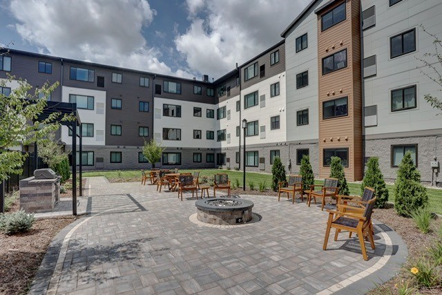 A courtyard with a fire pit and chairs surrounded by apartment buildings.