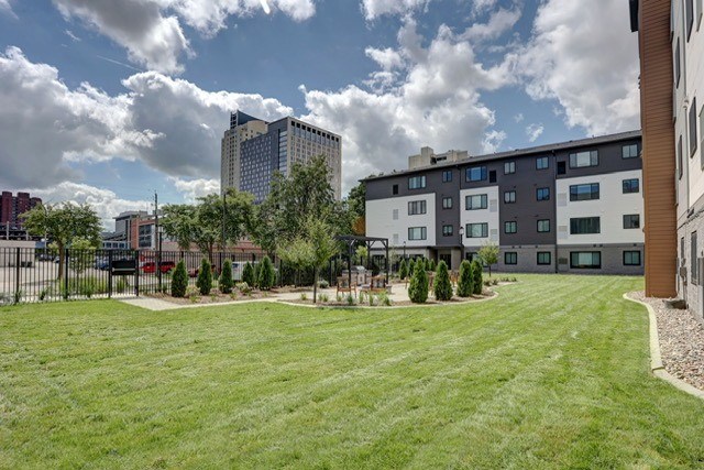 A large grassy area in front of a building with trees and a fence.