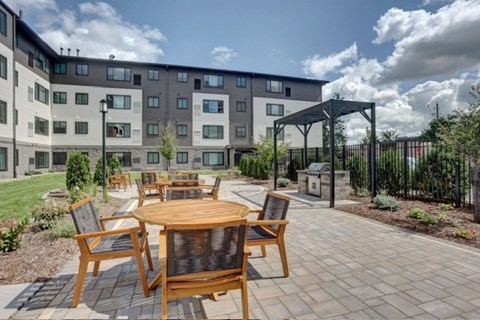 A patio with a table and chairs is surrounded by a grassy area and a building.