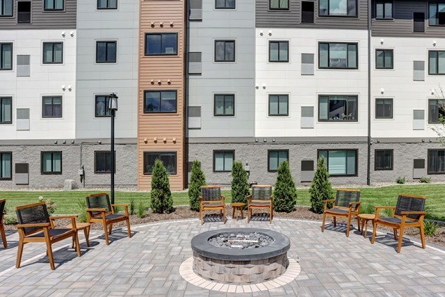 A fire pit sits in the middle of a patio surrounded by wooden chairs.