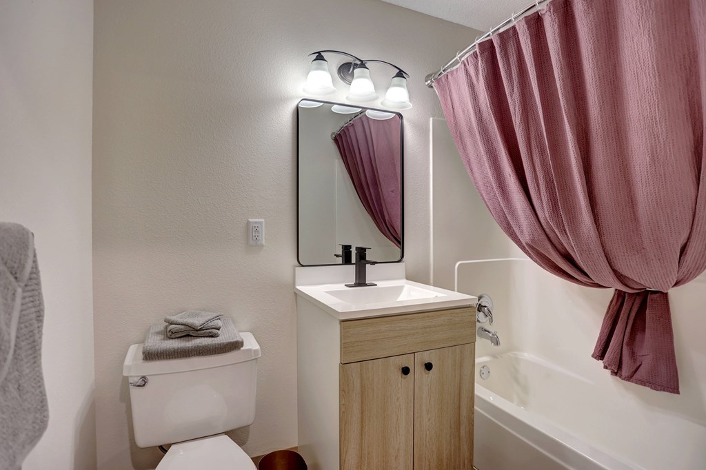 A bathroom with a toilet, sink, and a pink shower curtain.