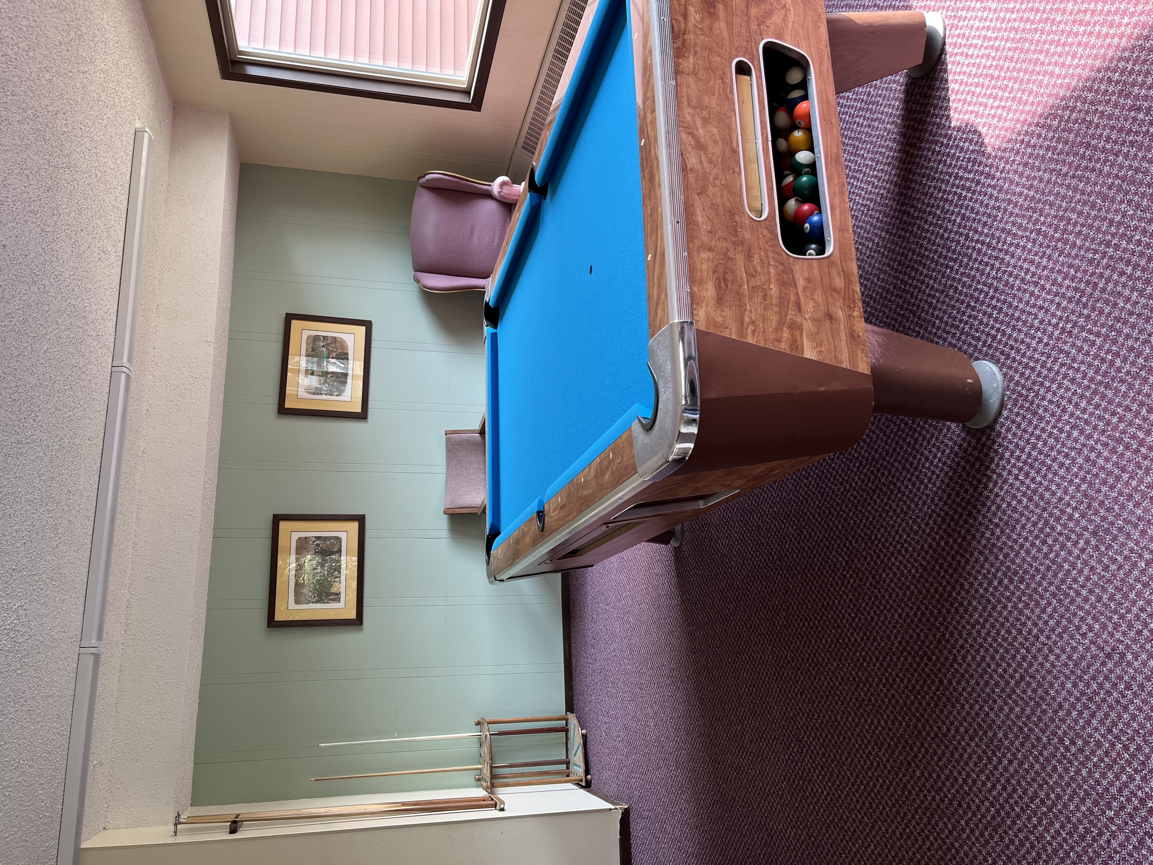 A pool table with a brown side rail and a blue felt cloth.