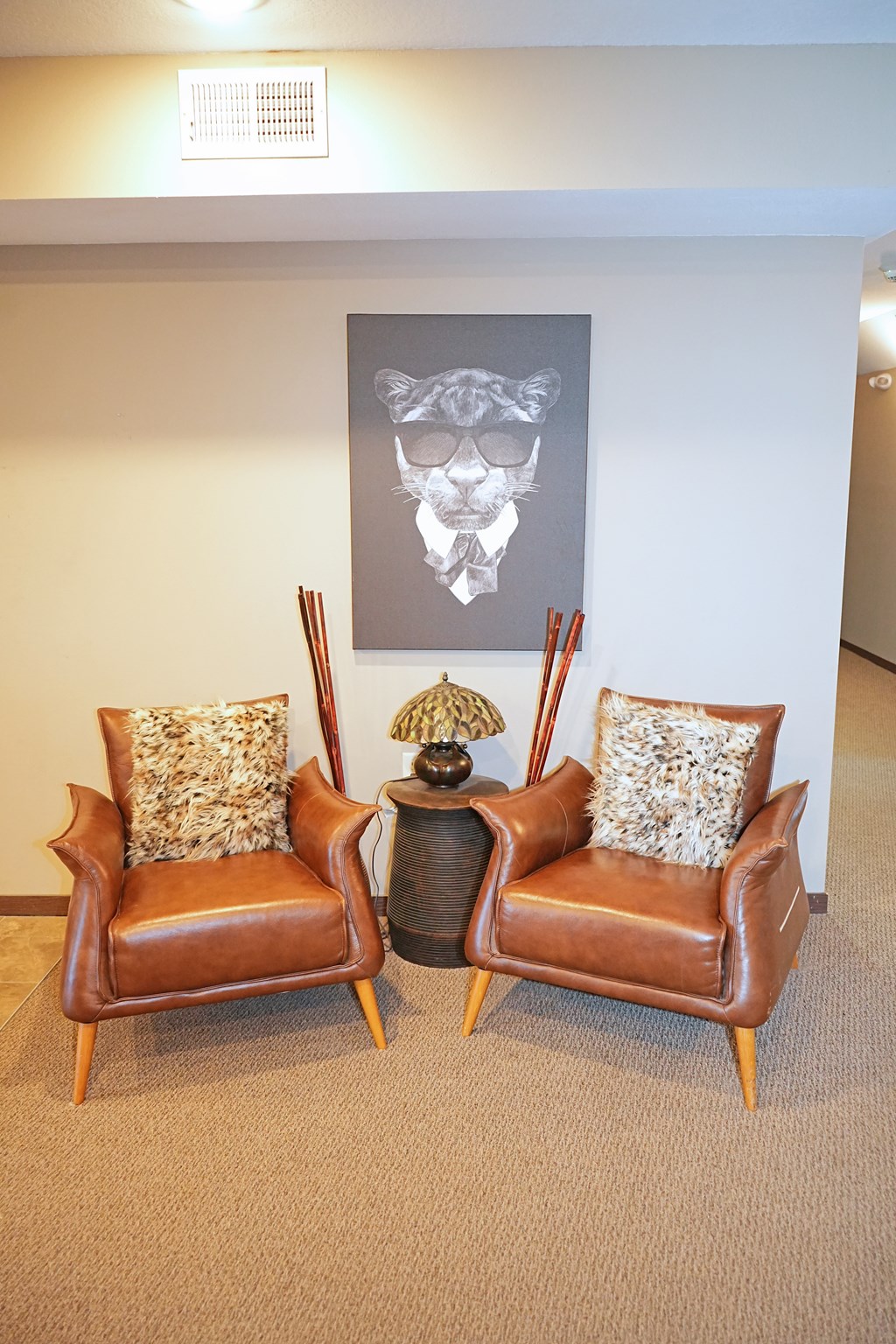 Two brown leather chairs with pillows and a table with a lamp between them.