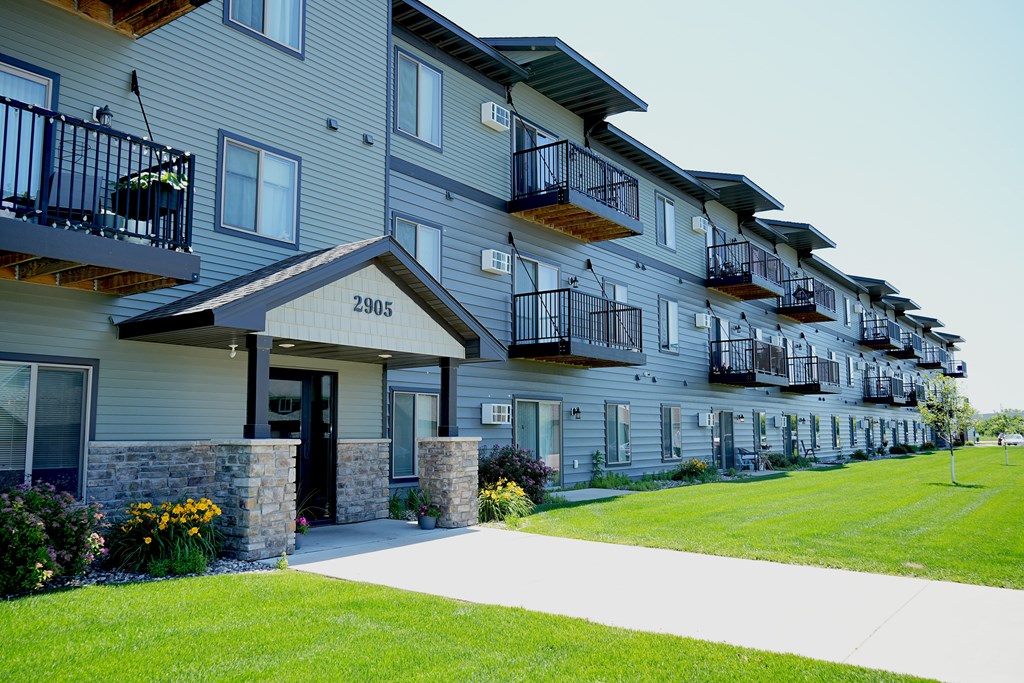 Apartment building with balconies and a green lawn in front.