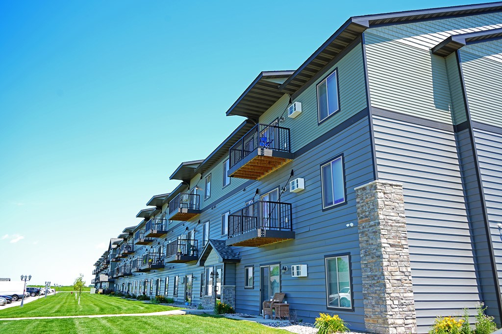 A long building with balconies and a green lawn in front.