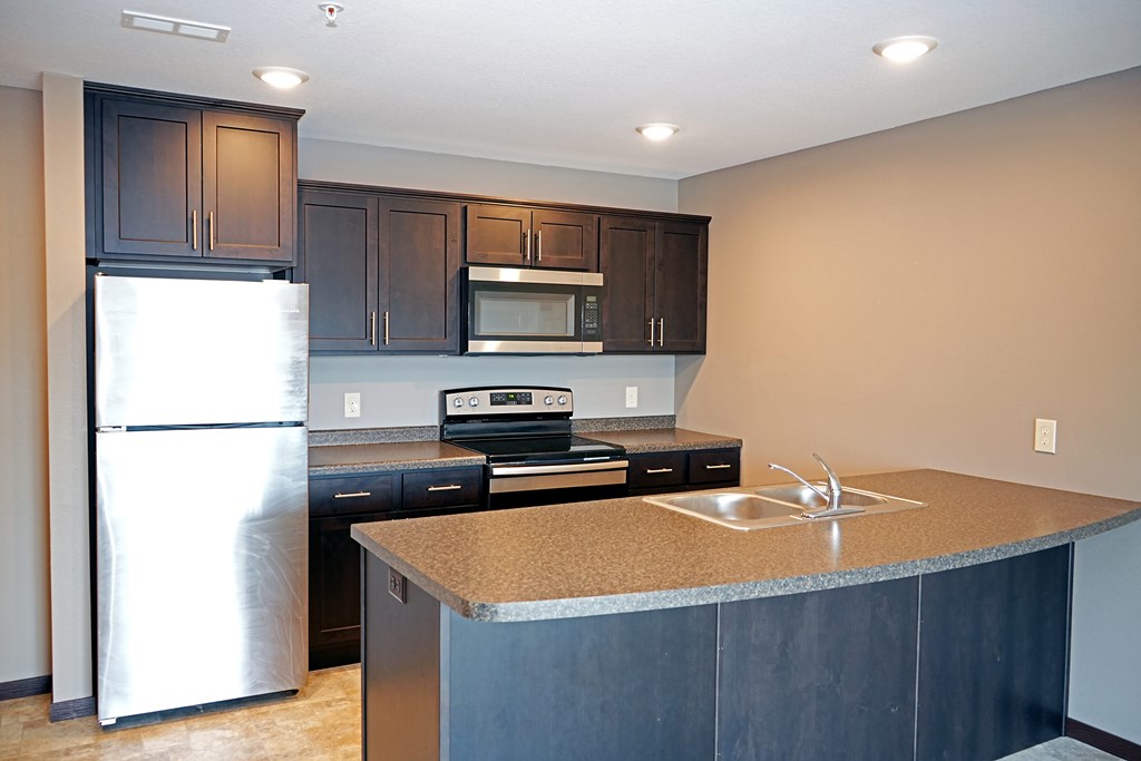 A kitchen with a refrigerator, microwave, oven, and sink.