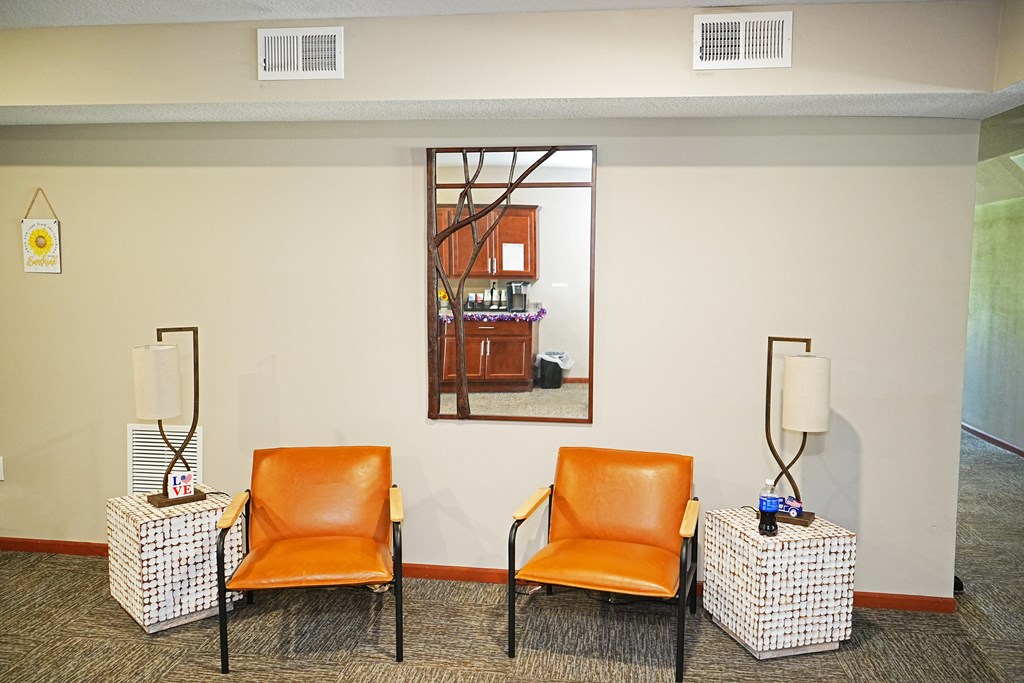 Two orange chairs are placed in front of a window with a view of a kitchen.