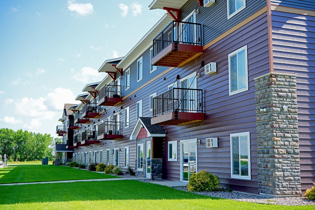 A row of houses with balconies and a green lawn in front.