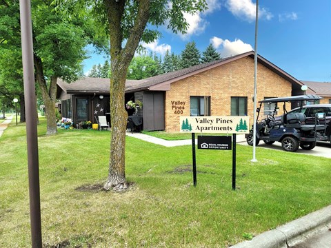 A sign for Valley Pines Apartments stands in front of a brick building.