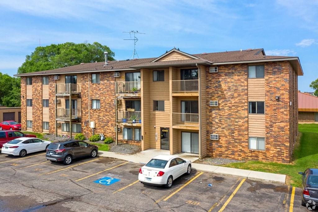 A parking lot in front of a brick apartment building with cars parked.