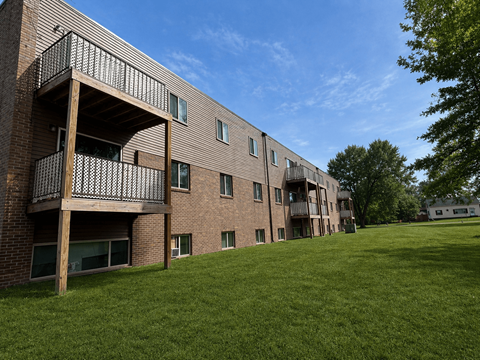 A large grassy area in front of a brick building with balconies.