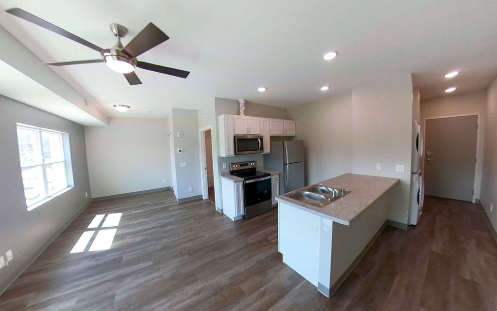 a living room with a kitchen and a ceiling fan