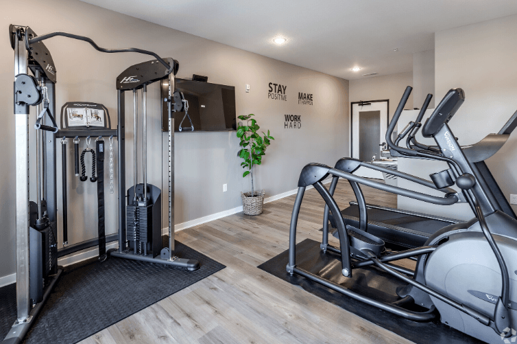 A gym with a row of treadmilers and a wall with the words "Stay Positive, Make Work Hard".