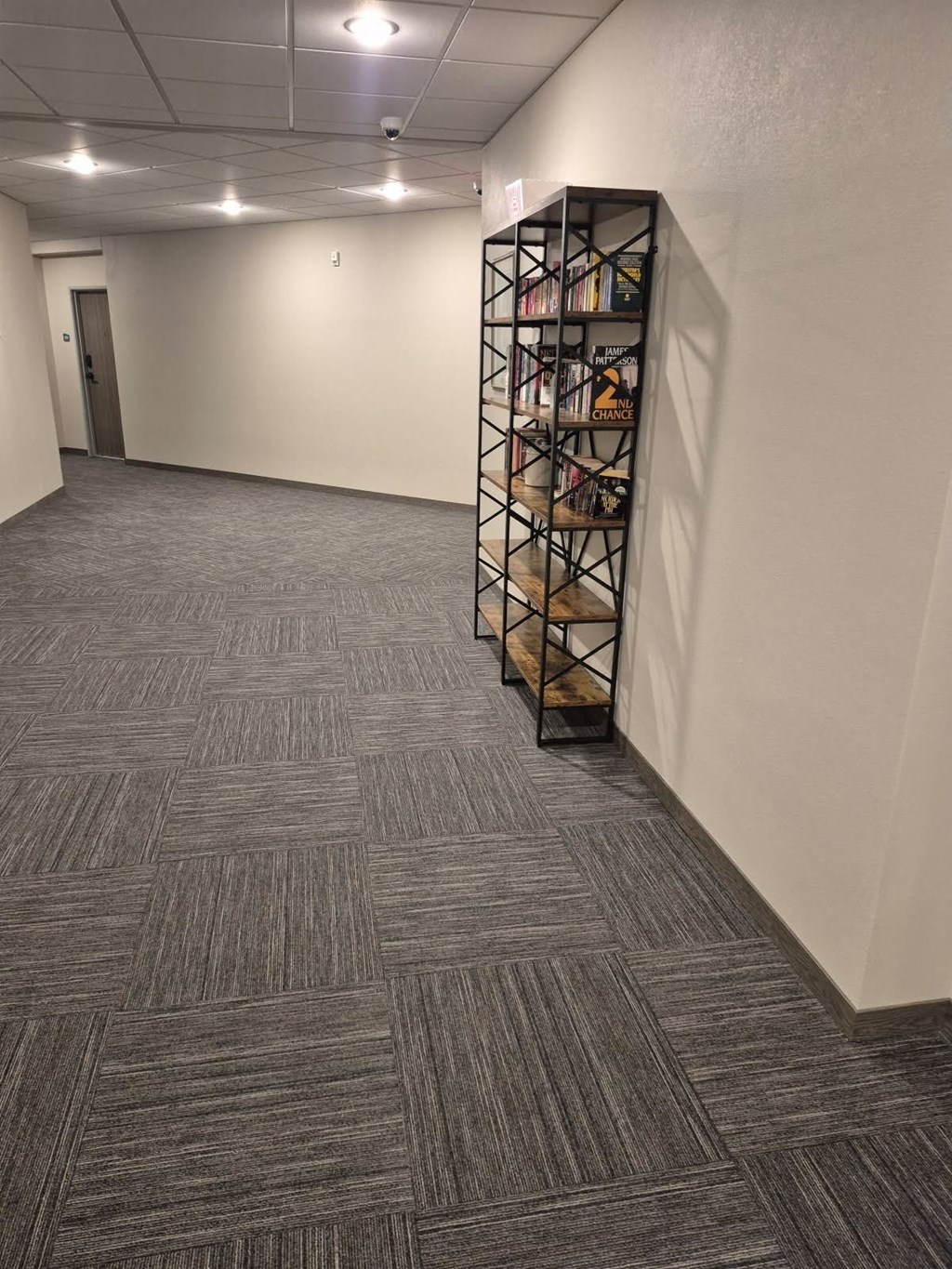 A hallway with a carpeted floor and a bookshelf on the right side.