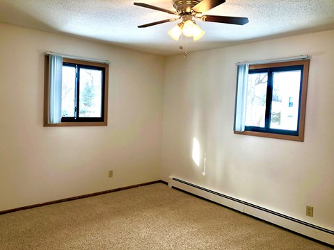 A room with a ceiling fan and two windows.
