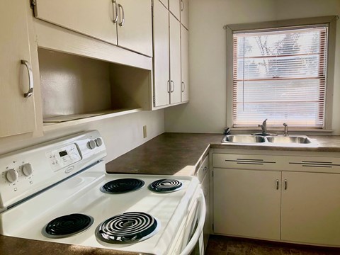 A white stove with four burners is in a kitchen with white cabinets.