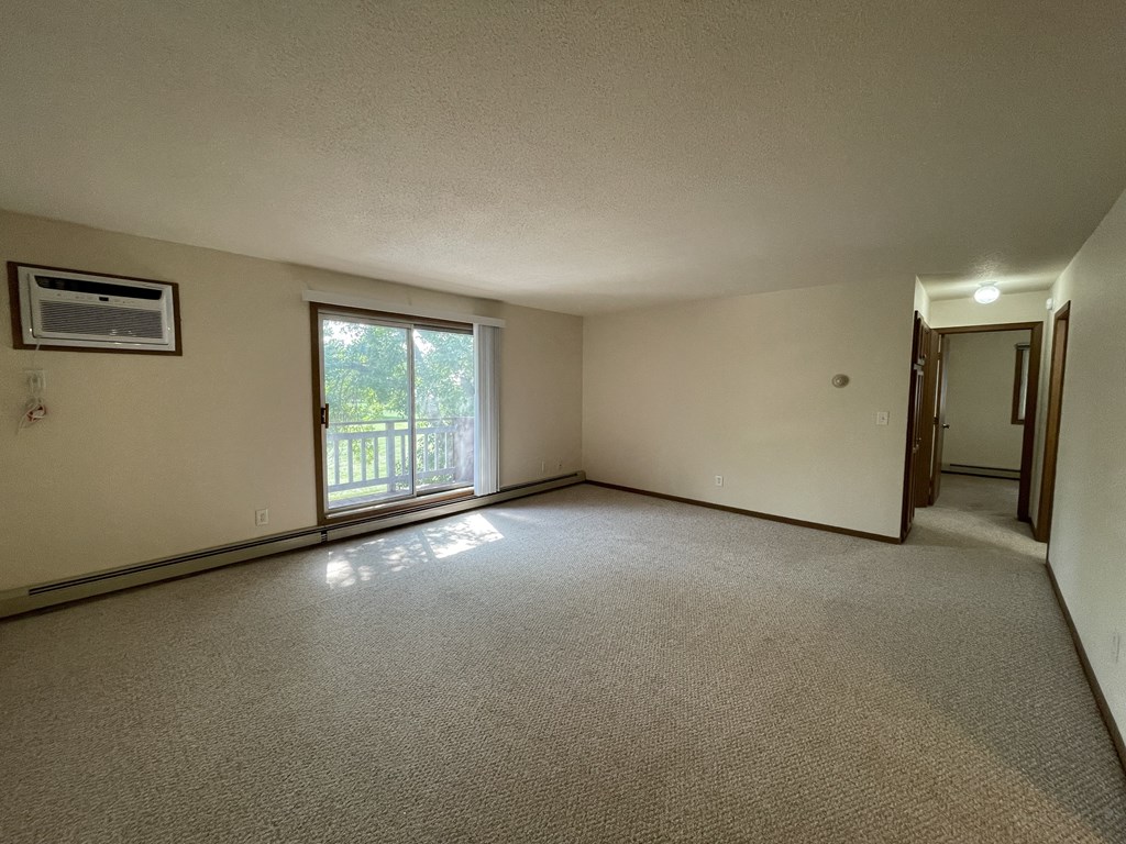 A room with a carpeted floor, a window with a view of trees, and a door leading to another room.