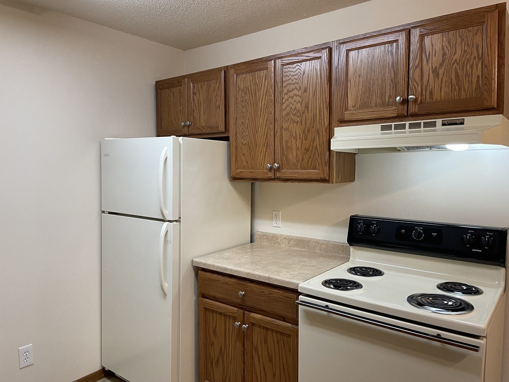 A kitchen with a white refrigerator, wooden cabinets, and a white stove top oven.