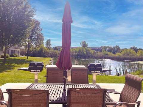 A patio with a table, chairs and an umbrella overlooking a pond.