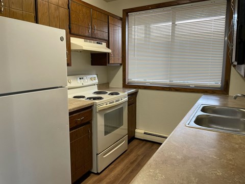 A kitchen with a white refrigerator, white oven, and a window with blinds.