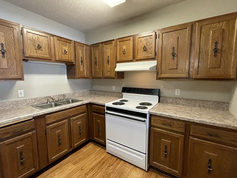 A kitchen with wooden cabinets and a white stove top oven.