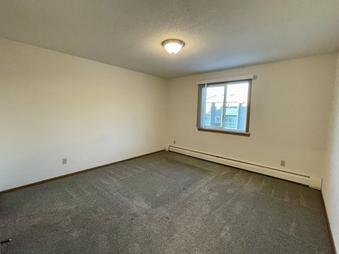 A room with a window and a grey carpet.