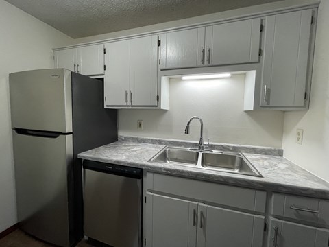 A kitchen with a black refrigerator and a marble counter top.