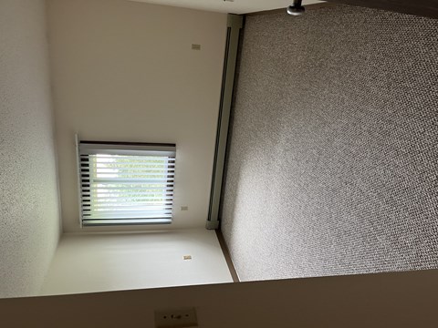 A window with blinds is on the left side of a room with a textured wall.