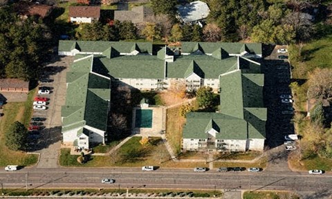 A large building with a green roof is surrounded by trees and a parking lot.