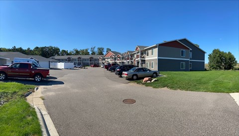 A residential street with houses on both sides and cars parked on the right.