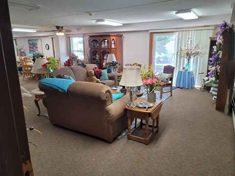 A living room with a brown couch and a table with a vase of flowers on it.