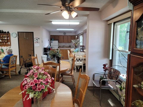 A dining room with a table and chairs and a woman sitting in a chair.