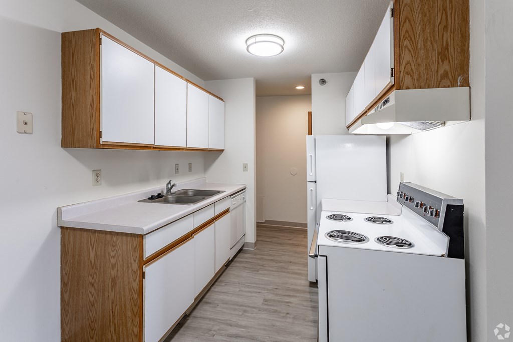 BLDG B/D - A kitchen with white appliances and wooden cabinets.