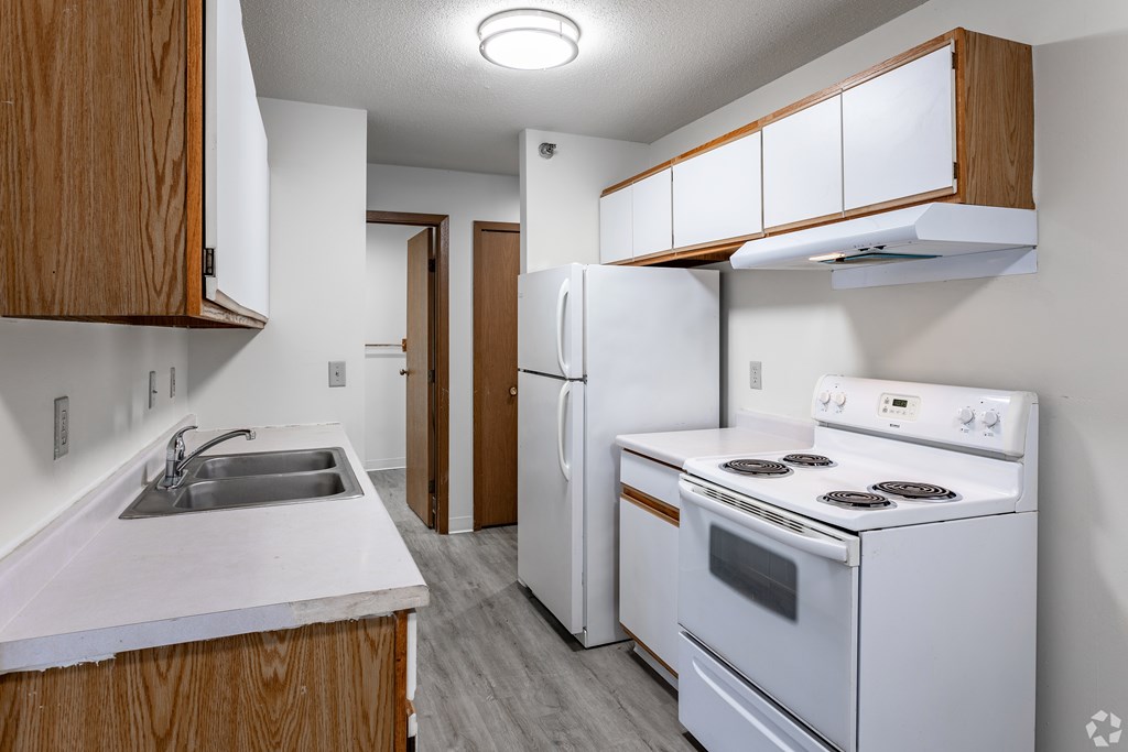 BLDG B/D - A kitchen with white appliances and wooden cabinets.