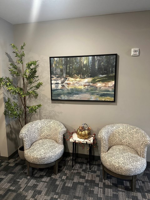 Two chairs sit in front of a framed picture of a forest.
