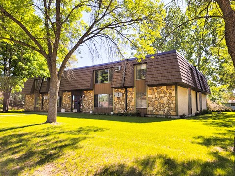 A house with a brown roof and a stone wall is surrounded by trees.